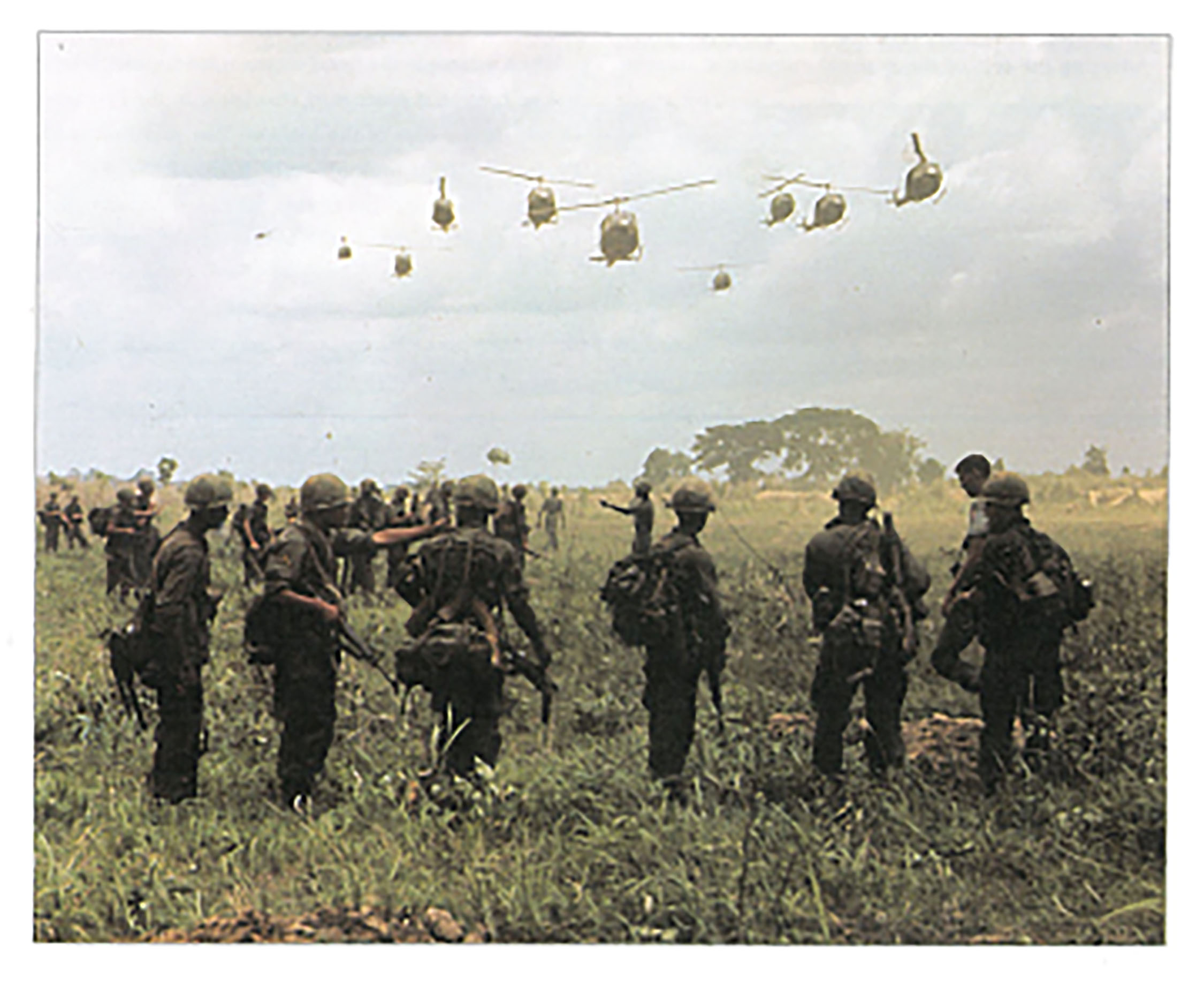Soldiers in a field watching military helicopters arrive.
