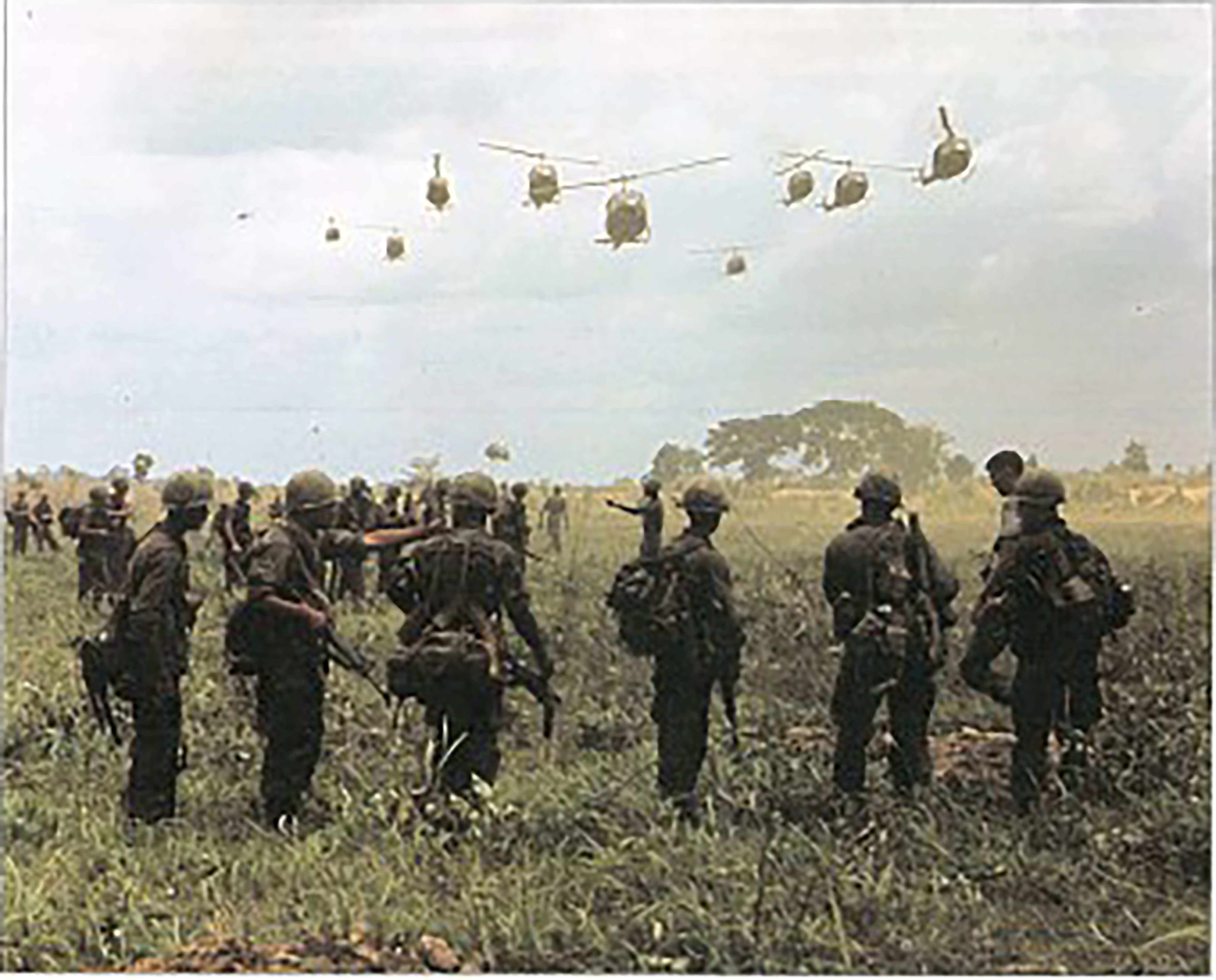 Soldiers in a field watching military helicopters arrive.