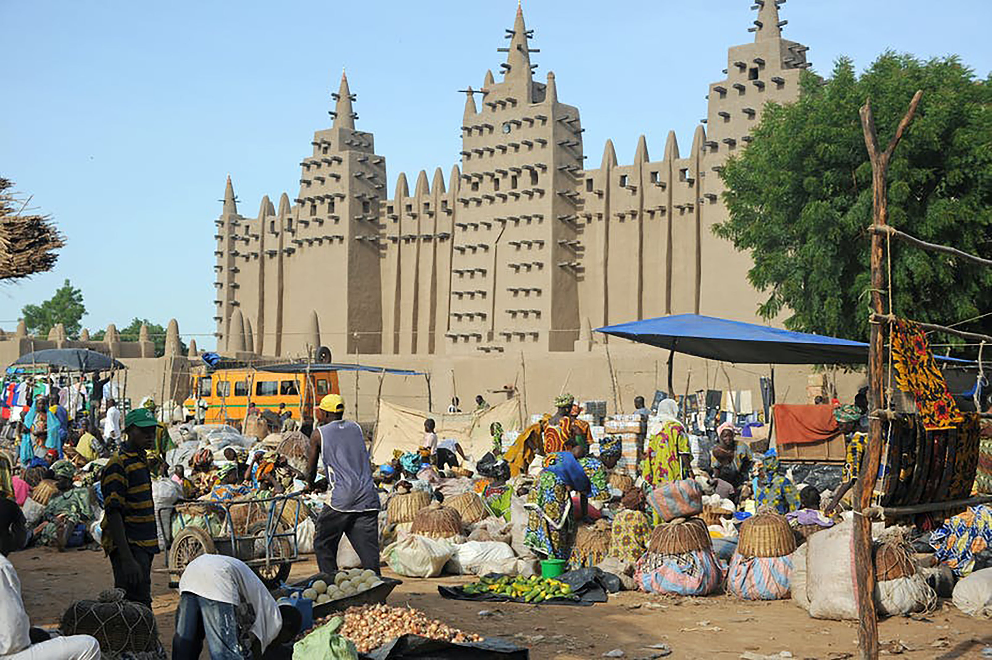 Painting of a West African Market that has push carts moving through melon tents, busses, and other market wares.