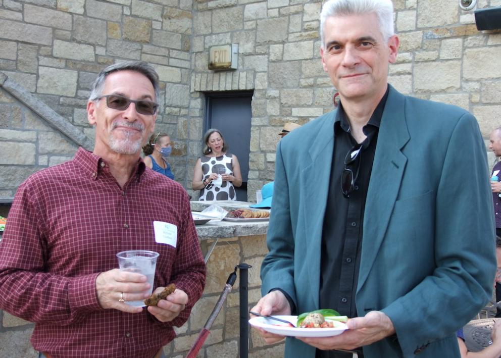 History professors at Convocation event smile for photo outside on Oread balcony. Professor on left is holding cup and cookie. Professor on left has plate of food.