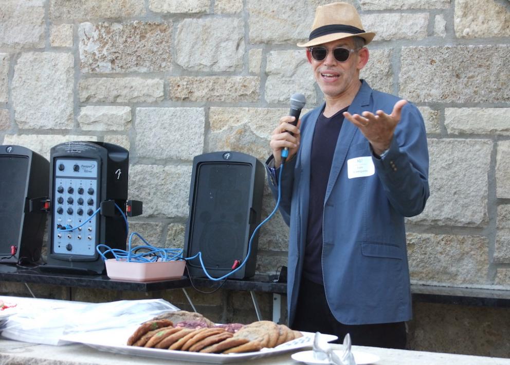History department chair speaks on microphone at the Convocation event on the Oread balcony. Plate of cookies is on table in foreground.