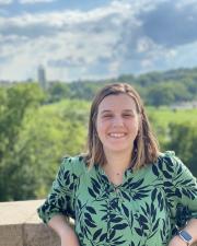 a woman with shoulder length hair wears a green shirt with a floral print as she smiles at the camera in a relaxed pose
