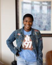 a woman standing with her hand in her pocket, smiling at the camera