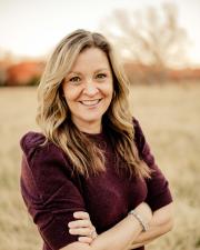 Image of a woman in a burgundy sweater, with her arms crossed, smiling at the camera. 