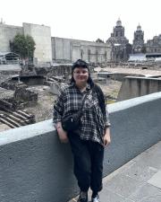 a travel image of a woman wearing a flannel shirt in front of the ruins of 
