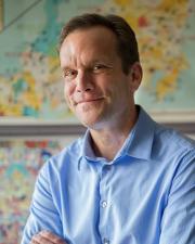 A man wearing a blue collared shirt with his arms crossed smiling at the camera