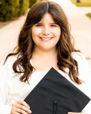 A woman smiling at the camera with a graduation cap displayed in hand