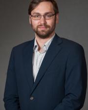 a man in a blue suit with glasses posing for a professional headshot 
