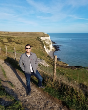 A man standing on a road smiling along a coast line