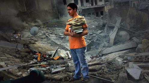 A boy saves a few books from the rubble of his home