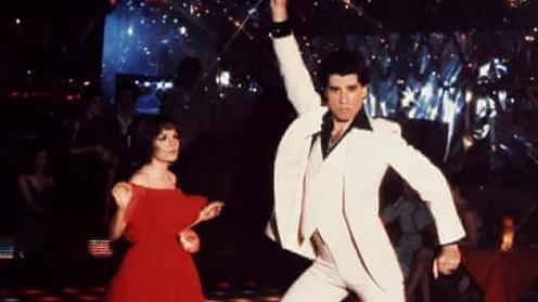 John Travolta striking a pose on a disco floor with his iconic disco suit. 
